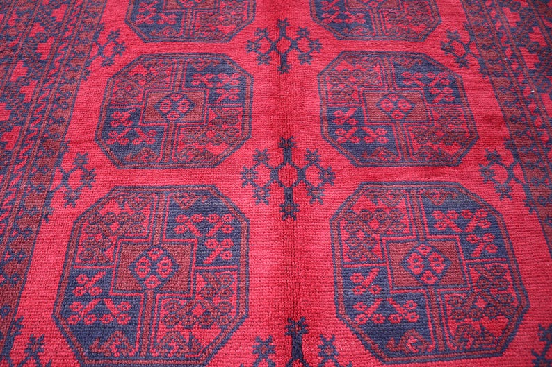 Puede incluir: Primer plano de una alfombra roja con un patr&oacute;n geom&eacute;trico repetitivo. El dise&ntilde;o presenta formas octogonales en tonos de rojo y azul oscuro, con detalles intrincados. La alfombra tiene una superficie texturizada.