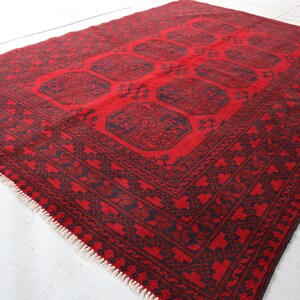 Puede incluir: Una alfombra rectangular roja con un borde oscuro y un dise&ntilde;o central. La alfombra presenta un patr&oacute;n geom&eacute;trico repetitivo en rojo oscuro y negro. La alfombra tiene una franja en un borde.