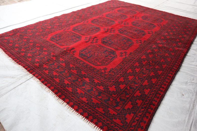 Puede incluir: Una alfombra rectangular roja con un borde oscuro y un dise&ntilde;o central. La alfombra presenta un patr&oacute;n geom&eacute;trico repetitivo en rojo oscuro y negro. La alfombra tiene una franja en un borde.