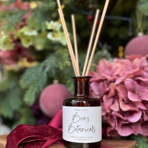 May include: A brown glass bottle diffuser with wooden sticks, labelled "Bea's Botanicals - Dark Honey - Tobacco, Sweet Honey and Patchouli"