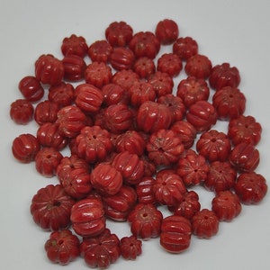 May include: A pile of red coral beads with a flower-like design. The beads are all different sizes and shapes.