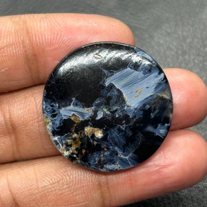 Könnte beinhalten: Ein runder, blauer und schwarzer Edelstein-Cabochon mit einem wirbelnden Muster. Der Stein hat einen metallischen Glanz und ist in einer silbernen Fassung gefasst.