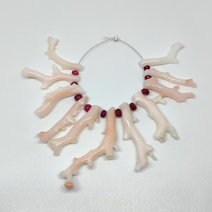 May include: A necklace featuring coral-shaped beads in shades of pink and white, strung together with small, round, red beads. The coral beads have a smooth, glossy finish and are arranged in a circular pattern.