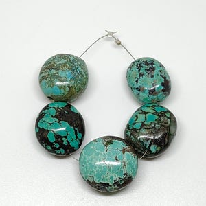 Könnte beinhalten: Eine Kette aus sechs Türkisperlen. Die Perlen sind oval geformt und haben eine Mischung aus Türkis und dunkelbraunen Farben. Die Perlen sind mit einem dünnen, silberfarbenen Draht aufgefädelt.