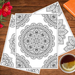 May include: Two black and white mandala coloring pages with intricate designs. The pages are on a wooden surface.