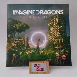 May include: A vinyl record album cover featuring a green, lush, overgrown cityscape with a person walking through a ring of light. The album cover is for Imagine Dragons' album "Origins". A wooden sign with the text "Chill Out" is in front of the album cover.