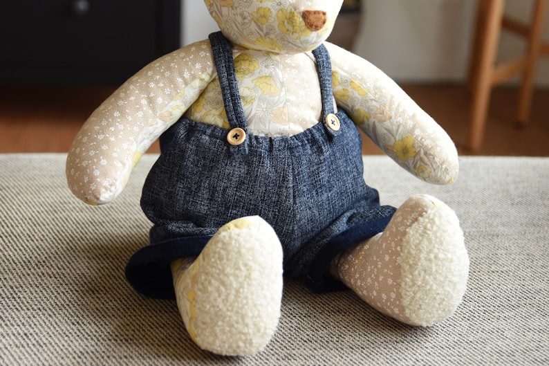 Puede incluir: Un oso de peluche hecho a mano con un cuerpo estampado floral y un peto vaquero. Los brazos y las piernas del oso est&aacute;n hechos de una tela color crema con peque&ntilde;as flores blancas. El peto tiene cierres de bot&oacute;n de madera. Un juguete encantador y artesanal.