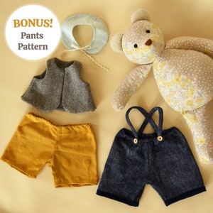 May include: A set of doll clothes including a brown and white vest, a pair of yellow shorts with brown polka dots, and a pair of blue denim overalls with brown buttons. The doll clothes are laid out on a beige surface next to a floral patterned teddy bear.