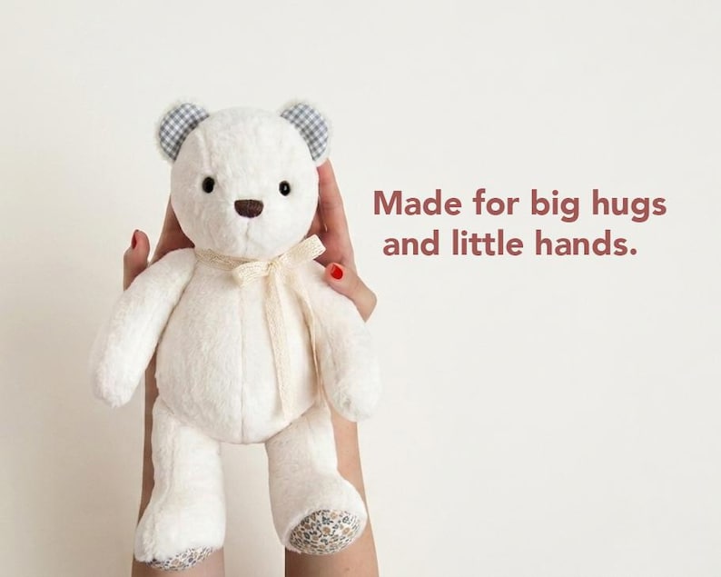 May include: A cream-coloured plush teddy bear with dark eyes and a brown nose. The bear features blue and white gingham inner ears, floral patterned foot pads, and a cream ribbon tied around its neck. The text reads: Made for big hugs and little hands.