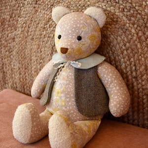 May include: A plush teddy bear with a floral pattern and a brown tweed vest. The bear is sitting on a brown corduroy surface.