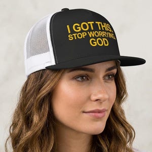 Może przedstawiać: Czarna i biała czapka typu trucker z napisem "I GOT THIS, STOP WORRYING, GOD" w złotym kolorze. Czapka ma siatkową tylną część i płaski daszek. Modny dodatek na co dzień.