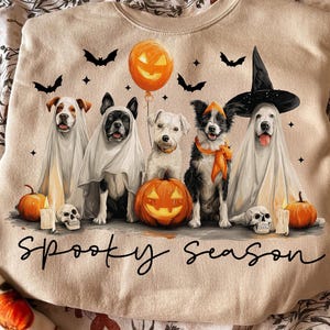 May include: Beige sweatshirt with a Halloween theme. Features five dogs dressed in costumes, including ghosts and a witch. Includes pumpkins, bats, candles, and the text "Spooky Season".