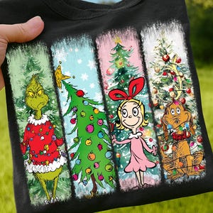 Op de afbeelding: Zwart T-shirt met een kerstontwerp verdeeld in vier verticale panelen. De panelen tonen personages en kerstbomen uit een vakantieverhaal. De Grinch, een kerstboom, Cindy Lou Who en Max de hond zijn afgebeeld.