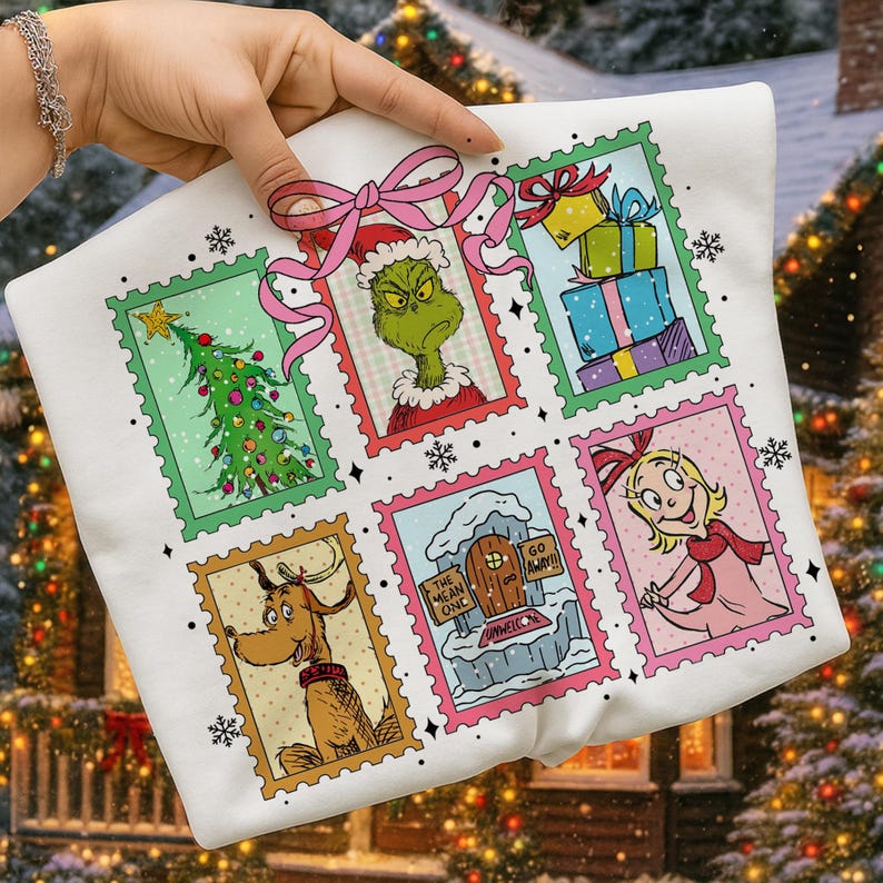 May include: White sweatshirt featuring a colorful Christmas-themed design. The design includes six postage stamp-style illustrations of characters and elements from a holiday story, with a pink bow at the top.