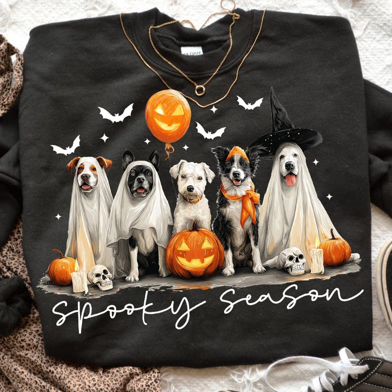 May include: Black sweatshirt featuring five dogs dressed in Halloween costumes. The dogs are surrounded by pumpkins, bats, and candles. The phrase "Spooky Season" is written in white script across the bottom.