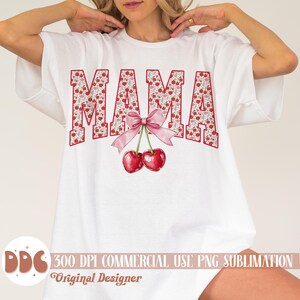 May include: White t-shirt with the word "MAMA" in red letters filled with a floral pattern. A pink bow and two red cherries are below the word. The shirt also has the text "300 DPI COMMERCIAL USE PNG SUBLIMATION Original Designer".