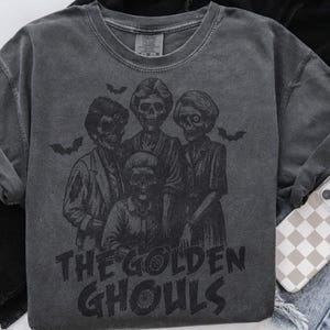 Puede incluir: Sudadera gris oscuro con un gr&aacute;fico de cuatro figuras esquel&eacute;ticas y murci&eacute;lagos, con el texto "THE GOLDEN GHOULS". La sudadera de cuello redondo tiene mangas largas, perfecta para Halloween o una est&eacute;tica espeluznante.