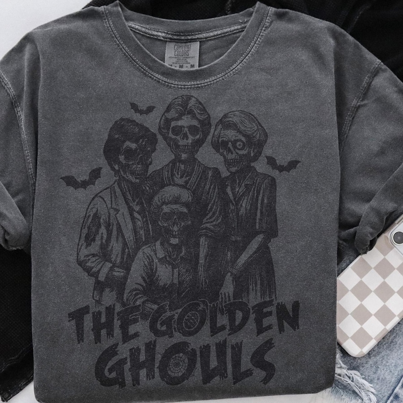Puede incluir: Sudadera gris oscuro con un gr&aacute;fico de cuatro figuras esquel&eacute;ticas y murci&eacute;lagos, con el texto "THE GOLDEN GHOULS". La sudadera de cuello redondo tiene mangas largas, perfecta para Halloween o una est&eacute;tica espeluznante.