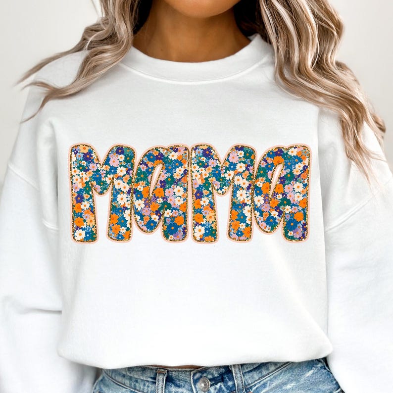 May include: White sweatshirt with the word "Mama" in large, colorful letters. The letters are covered in a floral pattern with orange, blue, and pink flowers.