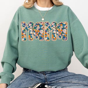 May include: A sage green sweatshirt with a floral print of the word "Mama" on the front.
