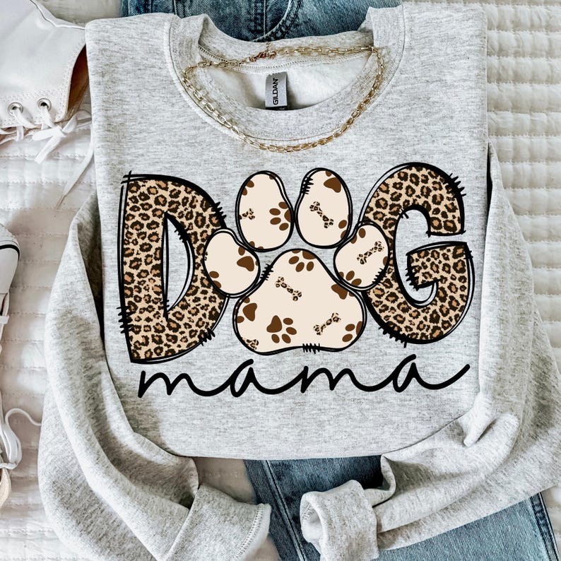 Pu&ograve; includere: Una felpa grigia con un design "DOG" a stampa leopardata con un'impronta di zampa al centro e la parola "mama" sotto.