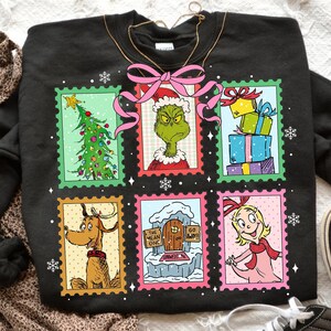 May include: Black sweatshirt featuring six colorful postage stamp designs with characters and elements from a Christmas story. The stamps include a Christmas tree, a green character, gifts, a dog, a house, and a girl.