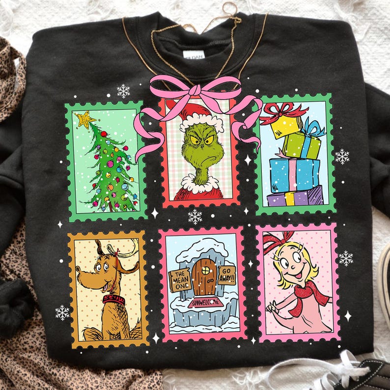 May include: Black sweatshirt featuring six colorful postage stamp designs with characters and elements from a Christmas story. The stamps include a Christmas tree, a green character, gifts, a dog, a house, and a girl.