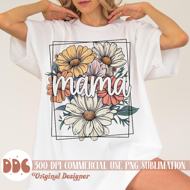 May include: White t-shirt featuring a floral design and the word "mama" within a black frame. The flowers are in shades of pink, yellow, and orange.