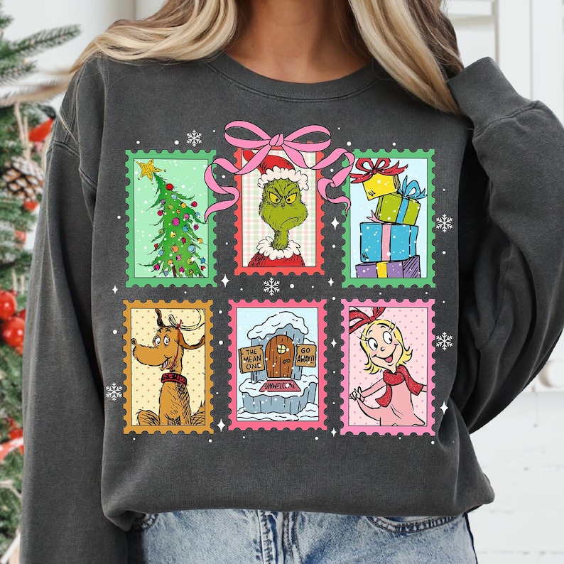 May include: Dark gray sweatshirt featuring a colorful graphic of Christmas-themed postage stamps. The stamps depict a Christmas tree, the Grinch, wrapped gifts, Max the dog, a sign that says "The Mean One", and Cindy Lou Who.