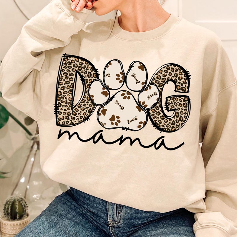 Pu&ograve; includere: Una felpa beige con una grafica "DOG" a stampa leopardata e un'impronta di zampa al centro. Il testo "mama" &egrave; scritto sotto la grafica.