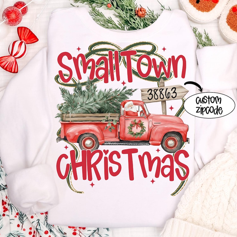 May include: White sweatshirt with a festive design. Features a red truck carrying a Christmas tree, with the words "Small Town Christmas" in red. Includes a custom zipcode option.