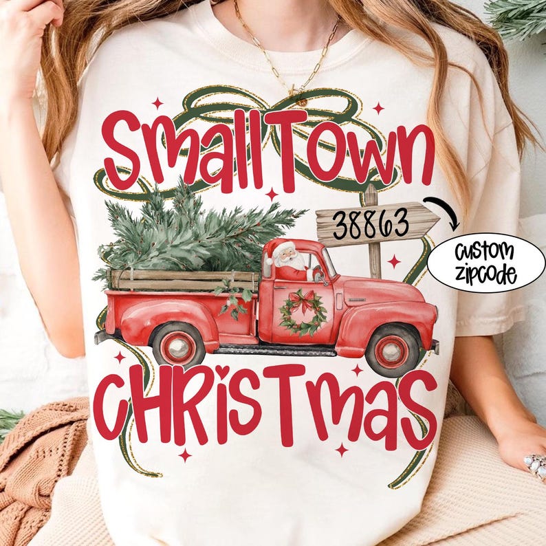 May include: Cream-colored t-shirt featuring a red vintage truck carrying a Christmas tree, Santa Claus, and the words "Small Town Christmas." The design includes a sign with the number 38863 and the words "Custom Zipcode."