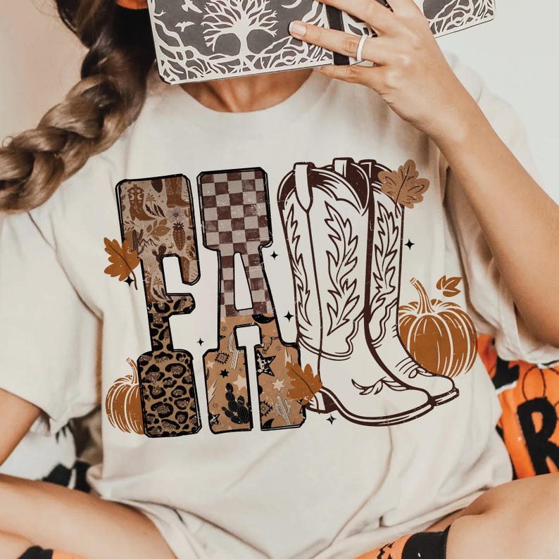 K&ouml;nnte beinhalten: Cremefarbenes T-Shirt mit dem Wort "FALL" in einem dekorativen Design. Die Buchstaben weisen Muster wie Leopardenmuster, Stiefel und ein Schachbrettmuster auf. Braune Cowboy-Stiefel, K&uuml;rbisse und Herbstbl&auml;tter vervollst&auml;ndigen die herbstliche Grafik.