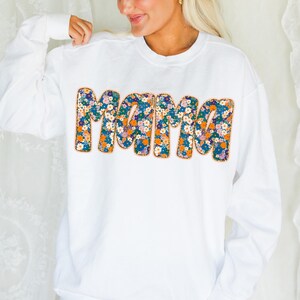 May include: White sweatshirt with a floral print of the word "Mama" in a retro style.
