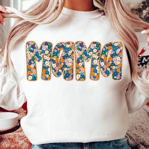 May include: White sweatshirt with the word "mama" spelled out in large, colorful letters. The letters are covered in a floral pattern with blue, orange, and pink flowers.