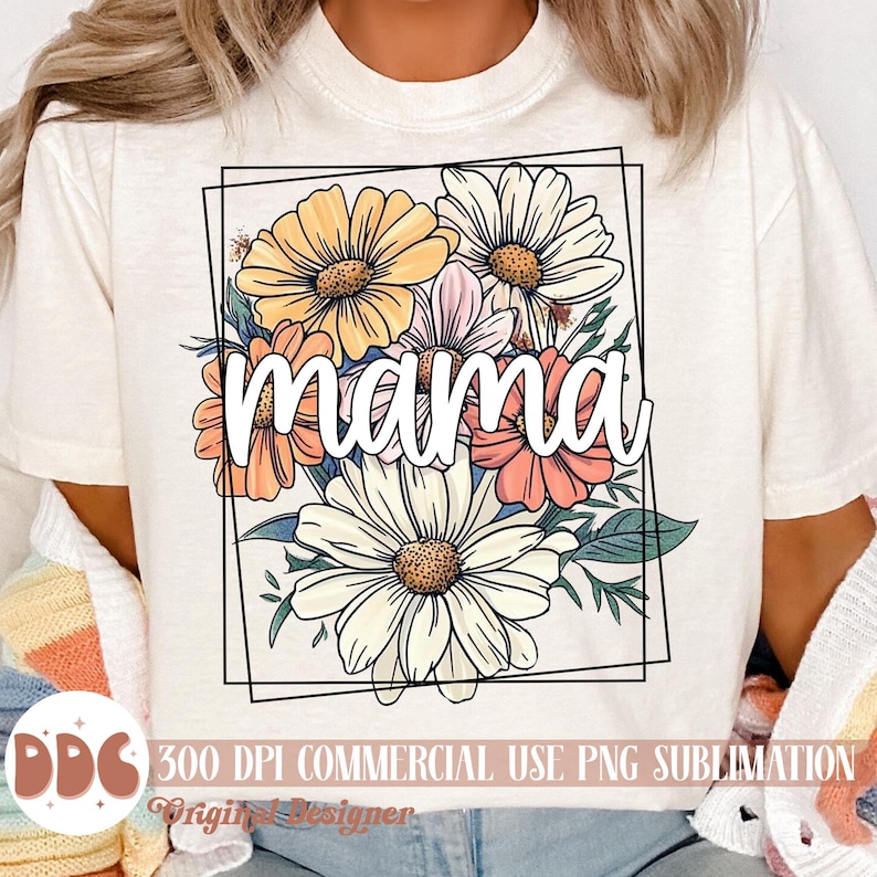 May include: A white t-shirt featuring a floral design and the word "mama" within a black frame. The flowers are yellow, pink, and white.