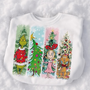 Op de afbeelding: Witte sweatshirt met een kleurrijk kerstthema. Het ontwerp toont de Grinch, een kerstboom, Cindy Lou Who en hond Max, elk in een apart verticaal paneel. De Grinch draagt een rode trui en Cindy Lou Who een roze jurk.