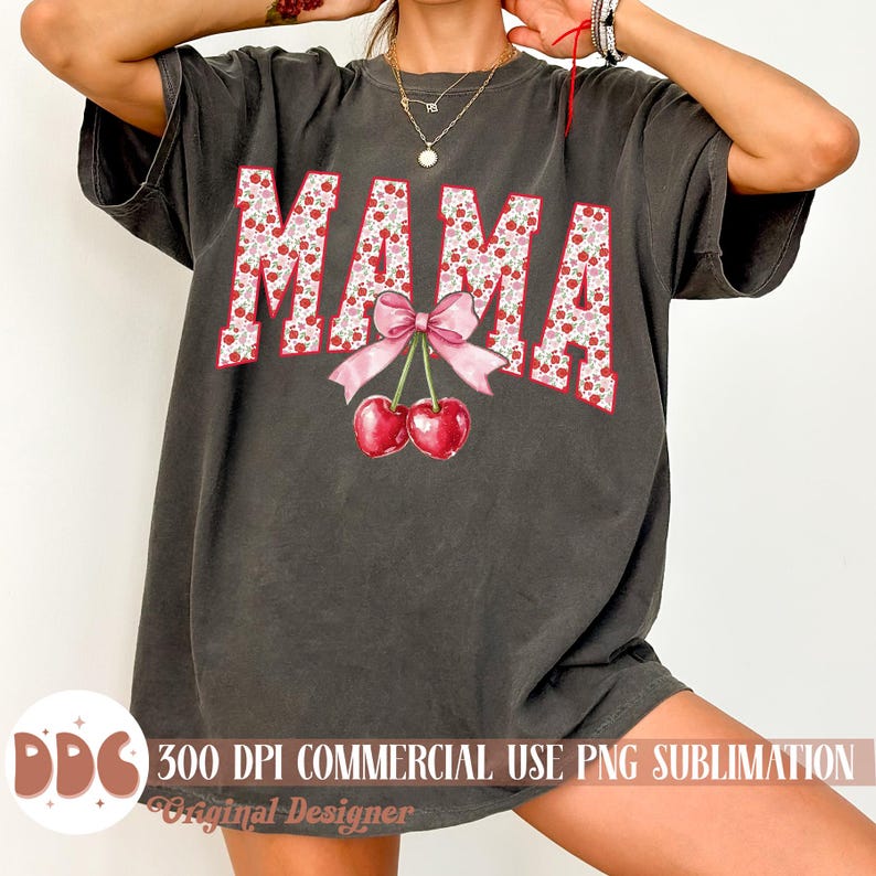 May include: Dark gray oversized t-shirt with the word "MAMA" in large, red letters filled with a floral pattern. A pink bow and two cherries are below the word. The shirt is a casual style.