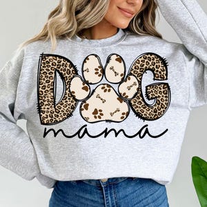 Pu&ograve; includere: Felpa grigia con un design "DOG" a stampa leopardata che presenta un'impronta di zampa con dettagli ossei e il testo "mama" sotto.