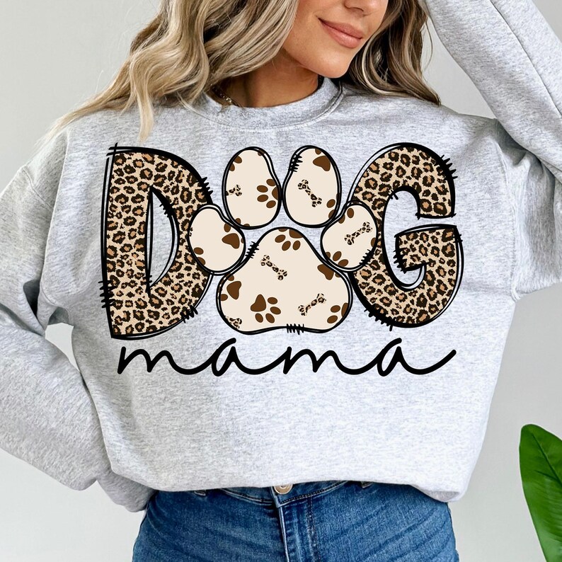 Pu&ograve; includere: Felpa grigia con un design "DOG" a stampa leopardata che presenta un'impronta di zampa con dettagli ossei e il testo "mama" sotto.