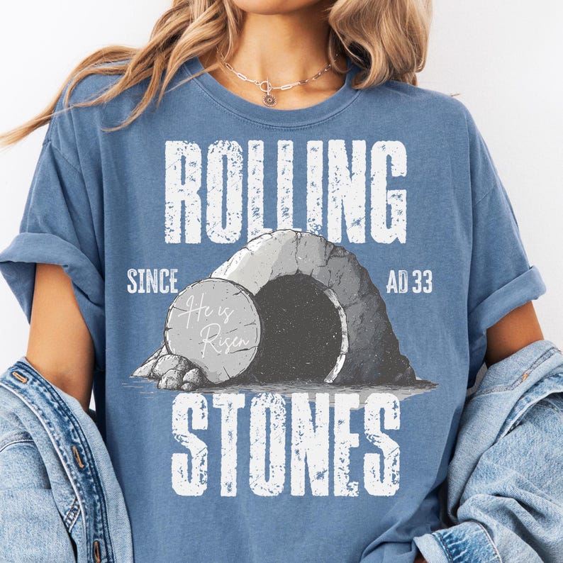 May include: A blue t-shirt with the words "ROLLING STONES" in large white letters. The shirt features a graphic of a tomb with a stone rolled away, and the text "He is Risen" on the stone. The shirt also has the text "SINCE AD 33".