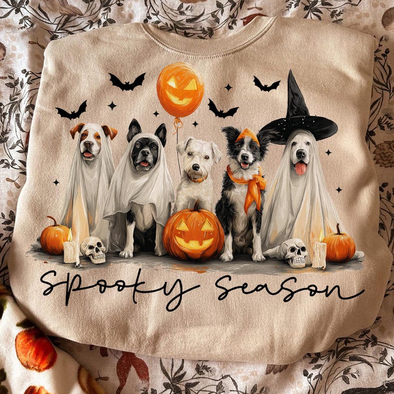 May include: Beige sweatshirt with a Halloween theme. Features five dogs dressed in costumes, including ghosts and a witch. Includes pumpkins, bats, candles, and the text "Spooky Season".
