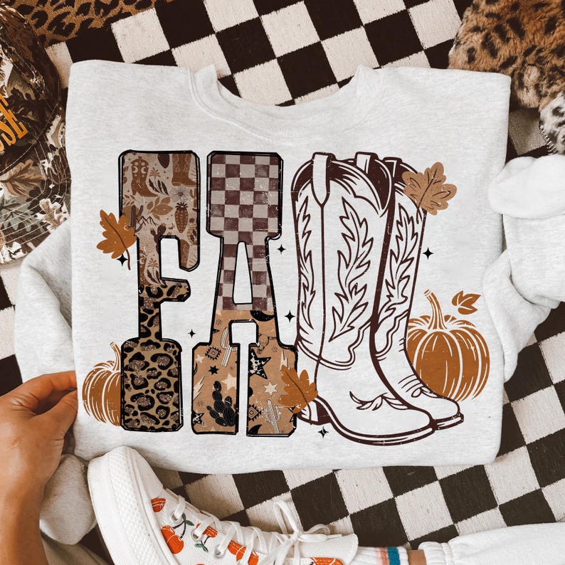 K&ouml;nnte beinhalten: Ein hellgraues Sweatshirt mit dem Wort "FA" in einer dekorativen Schriftart. Der Buchstabe "F" hat ein Leopardenmuster und der Buchstabe "A" hat ein Schachbrettmuster. Das Design umfasst Cowboy-Stiefel, K&uuml;rbisse und Herbstbl&auml;tter.