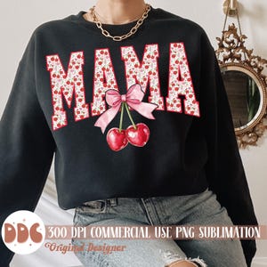 May include: Black sweatshirt with the word "MAMA" in a red and white floral pattern. A pink bow and two red cherries are centered below the word. The sweatshirt is a casual style.