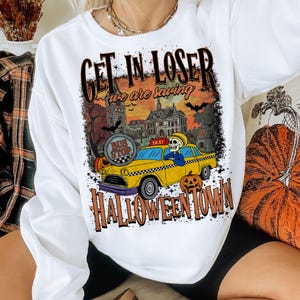 May include: White long-sleeve sweatshirt with a Halloween-themed graphic. The design features a yellow taxi with a skeleton driver, pumpkins, and the text "GET IN LOSER we are saving HALLOWEENTOWN".