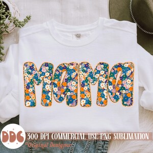 May include: A white sweatshirt with the word "Mama" in orange outlined letters. The letters are filled with a floral pattern of blue, orange, and white flowers.