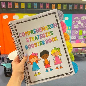 May include: A colorful spiral bound book with the title "Comprehension Strategies Booster Book". The book has tabs with different reading comprehension strategies, including "Predict", "Characters", "Check for Clues", "Cause & Effect", "Visualize", and "Compare".