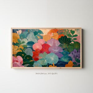 Op de afbeelding: Een rechthoekige wandkunstprint met een dichte, kleurrijke botanische illustratie van gestileerde waterleliebladeren en bloemen in tinten blauwgroen, oranje, roze, paars en rood. Het kunstwerk is ingelijst in een lichtgekleurde houten lijst.