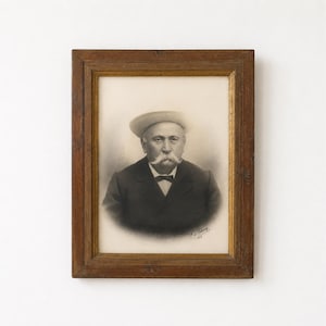 Peut inclure: Un portrait vintage en noir et blanc d'une personne avec une moustache proéminente portant un chapeau et un costume sombre, encadré dans un cadre en bois rectangulaire avec une bordure intérieure dorée. Le portrait porte une signature et 1902.