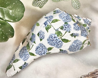 Könnte beinhalten: Eine weiße Muschel mit einem blauen und grünen Blumenmuster. Die Muschel ist mit einem Hortensienmuster verziert.